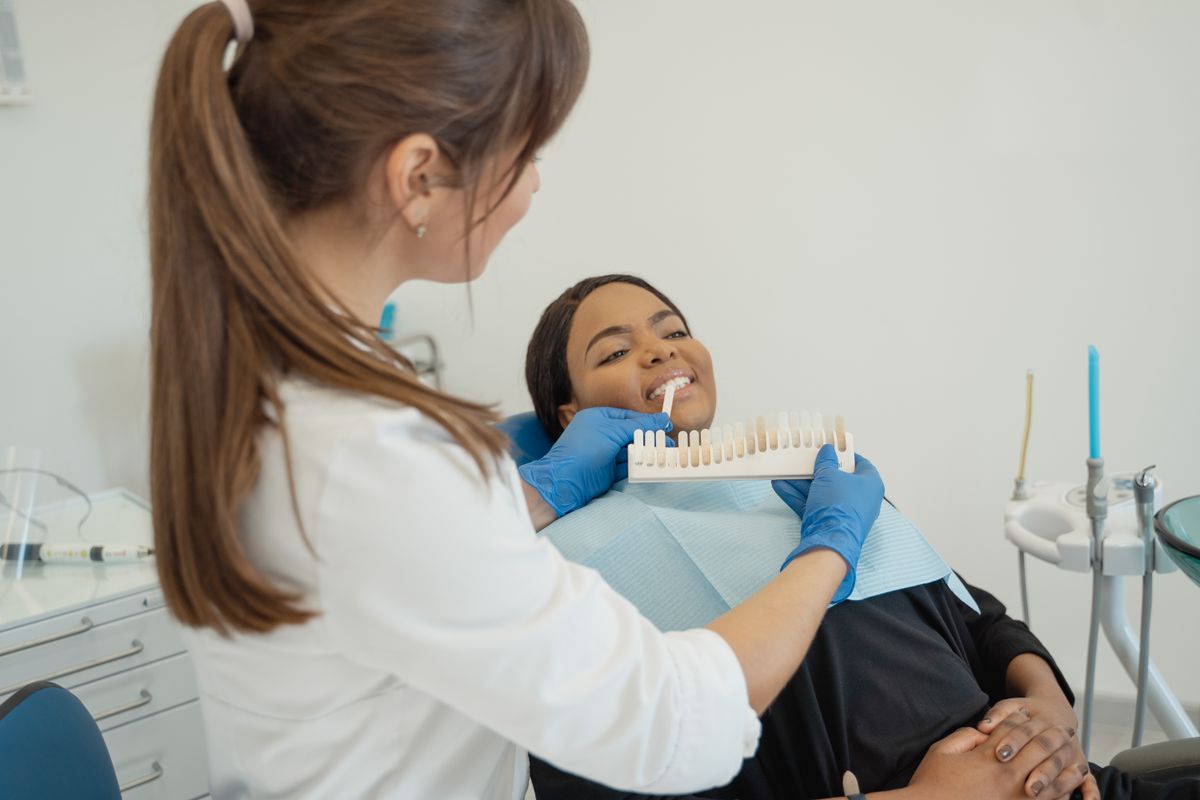 A dentist comparing a tooth shade guide with a patient’s smile.
